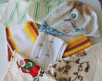May include: A collection of vintage kitchen towels in various designs and colors. Includes towels with green stripes, orange and brown stripes, floral patterns, and a Santa Claus design. Some towels have fringed edges.