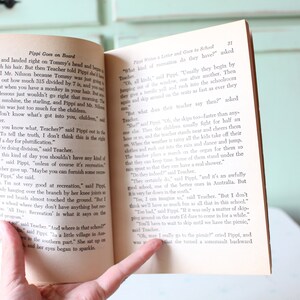 May include: Open book with a yellowed page showing a close-up of a hand holding the book open. The text on the page reads "Pippi Goes on Board" and "Pippi Writes a Letter and Goes to School".