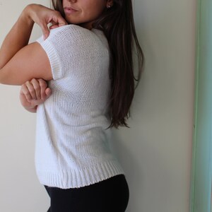 May include: A white knitted sweater with short sleeves. The sweater is loose fitting and has a slightly cropped length.