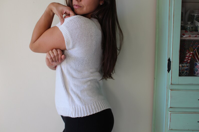May include: A white knitted sweater with short sleeves. The sweater is loose fitting and has a slightly cropped length.