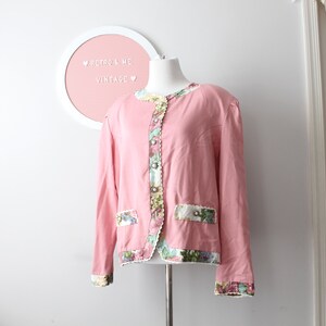 May include: A pink vintage jacket with floral trim and a white lace detail. The jacket has a button closure and long sleeves.