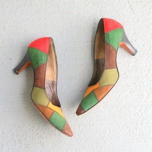 May include: A pair of high-heeled shoes with a patchwork design in shades of green, brown, orange, and red.