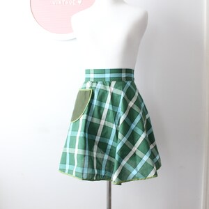 Pode incluir: Uma saia xadrez verde e azul com um bolso verde e uma bainha verde lim&atilde;o. A saia est&aacute; em um manequim branco.
