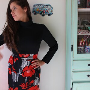 Peut inclure: Un haut noir &agrave; manches longues associ&eacute; &agrave; une jupe orn&eacute;e d'un motif floral audacieux en rouge et blanc sur fond noir. La tenue a une esth&eacute;tique vintage. Un bus VW bleu et blanc d&eacute;coratif est sur le mur.