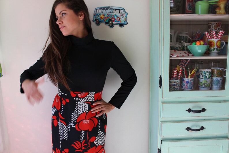 Peut inclure: Un haut noir &agrave; manches longues associ&eacute; &agrave; une jupe orn&eacute;e d'un motif floral audacieux en rouge et blanc sur fond noir. La tenue a une esth&eacute;tique vintage. Un bus VW bleu et blanc d&eacute;coratif est sur le mur.
