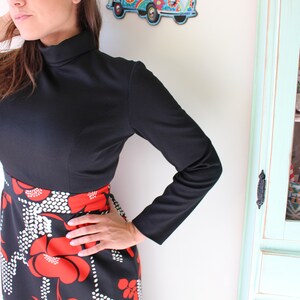 Peut inclure: Haut noir &agrave; manches longues avec un col montant, associ&eacute; &agrave; une jupe avec un fond noir et un motif floral rouge et blanc audacieux. L'ensemble est de style vintage.
