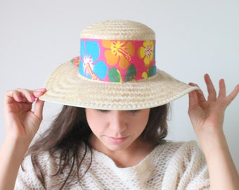 May include: A straw hat with a wide brim and a colorful floral band. The band features pink, blue, yellow, and green flowers.