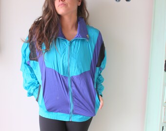 May include: A vintage teal, purple, and black windbreaker jacket with a full zipper closure. The jacket has a high collar and a color-blocked design. The sleeves are long and the jacket appears to be made of a lightweight material.