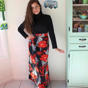 Peut inclure: Un haut noir &agrave; col roul&eacute; et une longue jupe orn&eacute;e d'un motif floral audacieux rouge et blanc sur fond noir. Le design de la jupe rappelle la mode vintage, parfait pour un look r&eacute;tro.