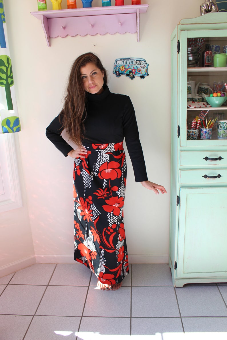 Peut inclure: Un haut noir &agrave; col roul&eacute; et une longue jupe orn&eacute;e d'un motif floral audacieux rouge et blanc sur fond noir. Le design de la jupe rappelle la mode vintage, parfait pour un look r&eacute;tro.