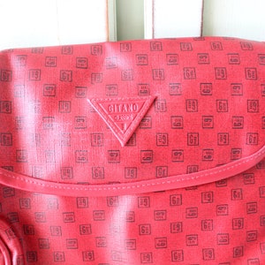 May include: Red leather shoulder bag with a black and white geometric pattern and a triangular logo that reads "Gitano Classics".