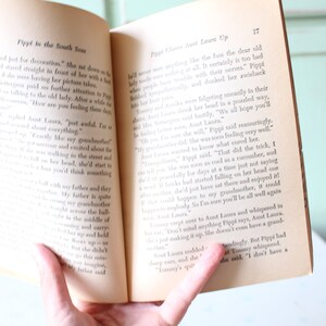 Peut inclure: Un livre ouvert avec une page jaunie montrant une histoire sur une jeune fille nomm&eacute;e Pippi. Le texte dit "Pippi dans les mers du Sud" et "Pippi grimpe chez tante Laura".