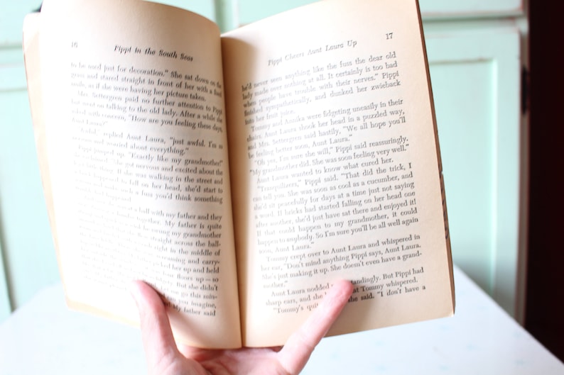 Peut inclure: Un livre ouvert avec une page jaunie montrant une histoire sur une jeune fille nomm&eacute;e Pippi. Le texte dit "Pippi dans les mers du Sud" et "Pippi grimpe chez tante Laura".