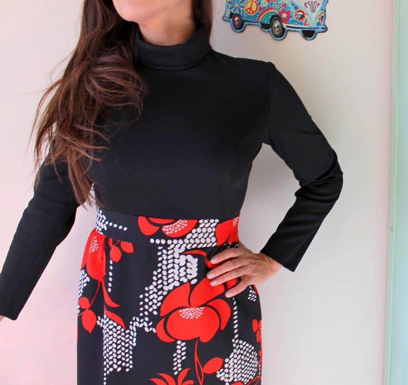 Peut inclure: Une robe noire &agrave; manches longues et col montant. La jupe pr&eacute;sente un motif floral audacieux en rouge et blanc sur fond noir. La robe a une coupe ajust&eacute;e.
