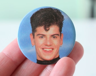 May include: A blue button with a photo of a man with dark hair and a blue background.