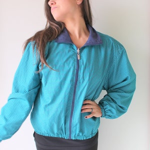 Könnte beinhalten: Eine blaue und marineblaue karierte Jacke mit Reißverschluss. Die Jacke hat einen Stehkragen und einen Gummizug am Saum.