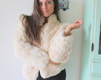 May include: A white faux fur jacket with a long sleeve and a collar. The jacket is worn by a person with long brown hair.