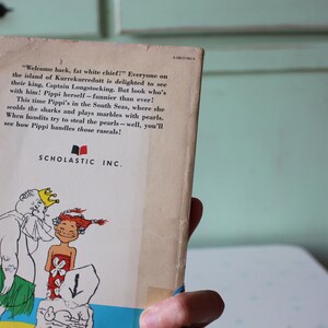 Peut inclure: La couverture arri&egrave;re d'un livre pour enfants illustrant un roi et une fille avec une couronne en dessin anim&eacute;. Le texte sur la couverture dit "Bienvenue, gros chef blanc !" Tout le monde sur l'&icirc;le de Kurrekurredutt est ravi de voir leur roi, le Capitaine Longstocking. Mais regardez qui est avec lui ! Pippi elle-m&ecirc;me - plus dr&ocirc;le que jamais ! Cette fois, Pippi est dans les mers du Sud, o&ugrave; elle gronde les requins et joue aux billes avec des perles. Quand des bandits essaient de voler les perles - eh bien, vous verrez comment Pippi s'occupe de ces voyous !" Le livre est publi&eacute; par Scholastic Inc.
