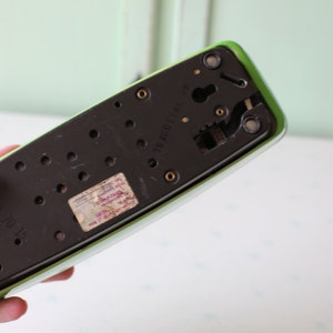May include: The bottom of a green rotary phone with a black dial and a label that reads "2X200/100".