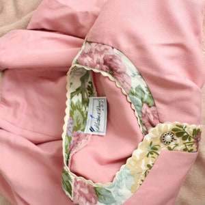 May include: A pink shirt with a floral trim and a white label that says "Mother & Paul" on it.