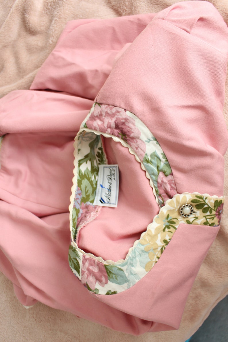 May include: A pink shirt with a floral trim and a white label that says "Mother & Paul" on it.