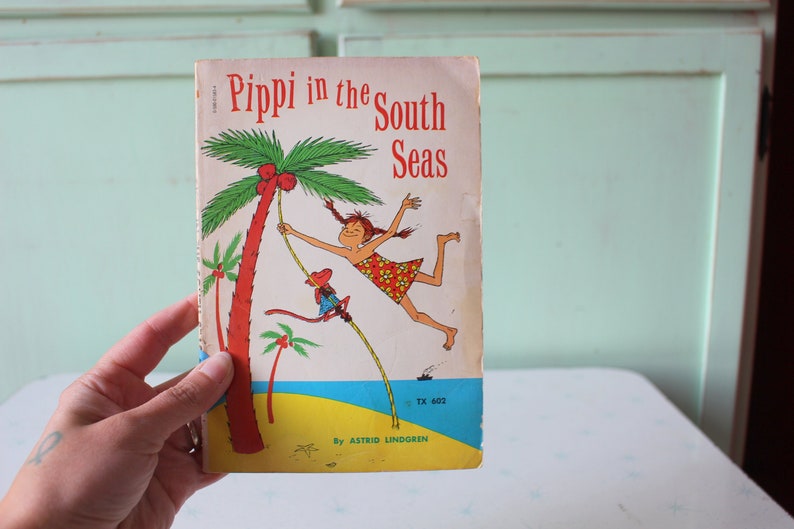 Peut inclure: Un livre pour enfants vintage intitul&eacute; "Pippi dans les mers du Sud" par Astrid Lindgren. La couverture pr&eacute;sente une illustration color&eacute;e d'une fille se balan&ccedil;ant sur un palmier avec un singe.