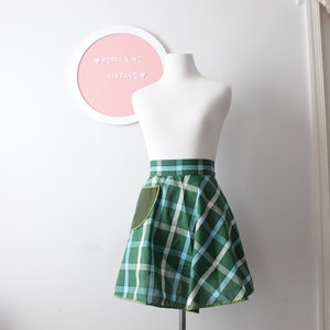 Pode incluir: Uma saia xadrez verde e azul com um bolso verde. A saia est&aacute; em um manequim branco e tem uma bainha amarela.