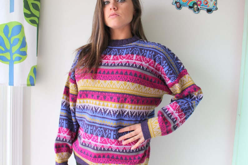 Puede incluir: Un su&eacute;ter a rayas de colores con un patr&oacute;n geom&eacute;trico en tonos de morado, rosa, azul, amarillo y blanco.