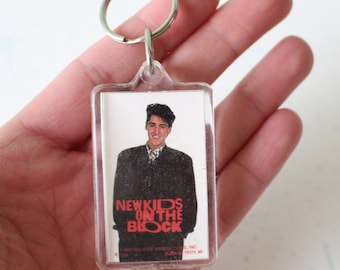 May include: A clear plastic keychain with a photo of a man in a black jacket and the words "New Kids on the Block" in red. The keychain is made by Step Productions, Inc.