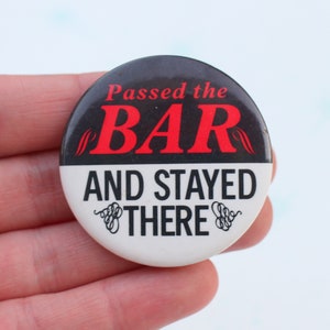 May include: A circular badge with a black upper section and a white lower section. The text "Passed the BAR" is in red, and "AND STAYED THERE" is in black. Decorative swirls are on the bottom half.