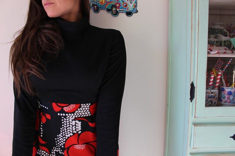 Peut inclure: Robe noire &agrave; manches longues avec un col montant et une jupe &agrave; motifs. La jupe pr&eacute;sente un fond noir avec des motifs floraux rouges et des pois blancs. La robe est de style vintage.