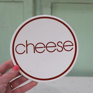 May include: White round ceramic cheese dish with a red rim and the word "cheese" written in red.