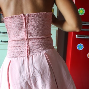 May include: A pink strapless dress with a gathered bodice and a full skirt. The dress has a zipper closure in the back.