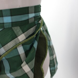 Pode incluir: Uma saia de embrulho xadrez verde, azul e branco com uma bainha verde. A saia &eacute; amarrada na cintura e tem um design longo e fluido.