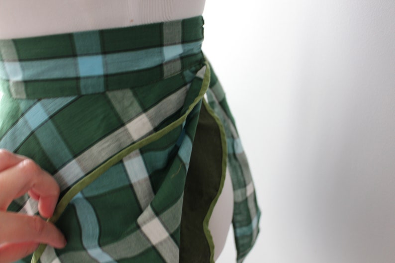 Pode incluir: Uma saia de embrulho xadrez verde, azul e branco com uma bainha verde. A saia &eacute; amarrada na cintura e tem um design longo e fluido.