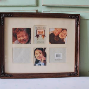 May include: A multi-photo picture frame with a dark brown wooden frame and decorative corner accents. The frame holds four photos and a central label. The photos include portraits of people. The label reads "INTERCRAFT".