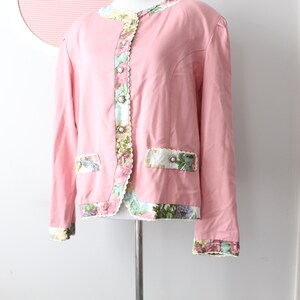 May include: A pink blazer with floral trim and a scalloped edge. The blazer has a button closure and two pockets.