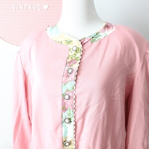 May include: A pink long-sleeved blouse with a floral print collar and decorative buttons down the front.
