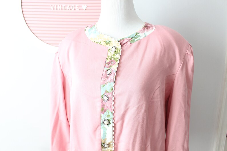 May include: A pink long-sleeved blouse with a floral print collar and decorative buttons down the front.