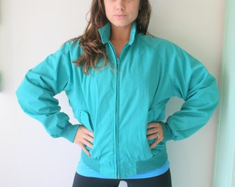 May include: A teal blue zip-up jacket with a stand-up collar. The jacket has a zipper closure and long sleeves.