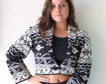 May include: A black and white cropped jacket with a geometric pattern. The jacket has a button closure and long sleeves.