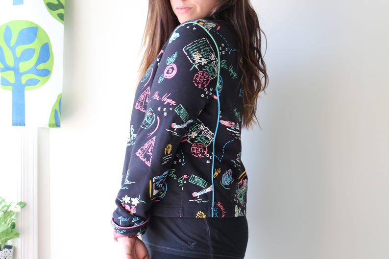 May include: A black long-sleeved shirt with a colorful print of geometric shapes, lines, and text. The shirt has a blue and green trim along the seams.