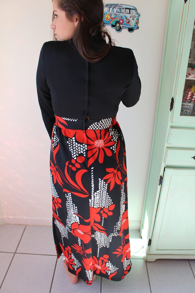 Peut inclure: Robe noire vintage avec un haut &agrave; manches longues et une jupe &agrave; imprim&eacute; floral. La jupe pr&eacute;sente un motif audacieux de fleurs rouges et d'accents blancs sur fond noir. La robe a un col montant et un corsage ajust&eacute;.