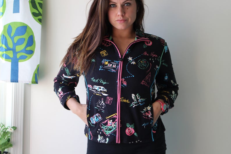 May include: Black zip-up jacket with a colorful print of travel-themed illustrations, including a road trip, a map, and the words "Be Happy".