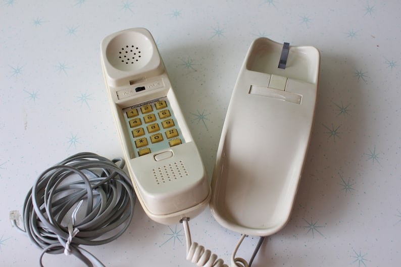 May include: A white rotary phone with a beige keypad and a coiled cord. The phone has a separate handset.