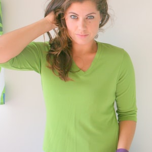 May include: A woman wearing a green, short-sleeved shirt with a v-neck. She is wearing a blue skirt with pink accents.