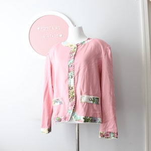 May include: A pink blazer with a floral trim around the collar, cuffs, and pockets. The blazer has a button closure and a white lining.