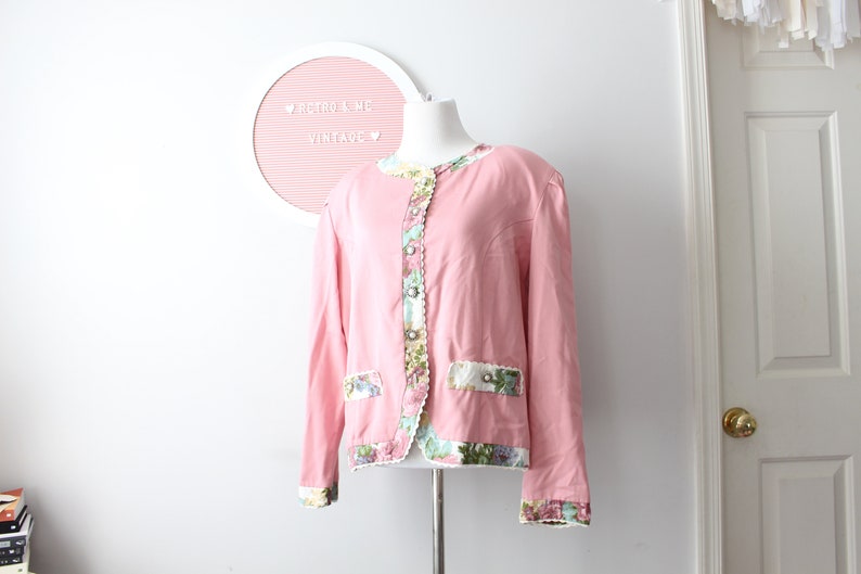 May include: A pink blazer with a floral trim around the collar, cuffs, and pockets. The blazer has a button closure and a white lining.