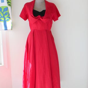 May include: A red dress with a black bow at the neckline. The dress has a full skirt and is on a mannequin.
