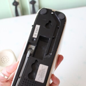 May include: White rotary phone with a black base and a black cord. The phone has a number "G 0491" printed on the back.
